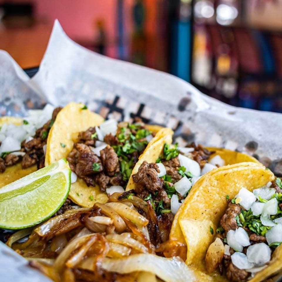 Mas Street Tacos with grilled meat, onions, cilantro, and a lime wedge in a basket.