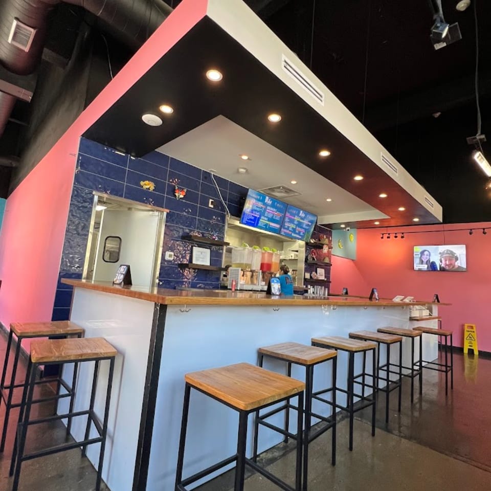 Mas Street Tacos' vibrant interior with a long bar, stools, and pink and blue walls.