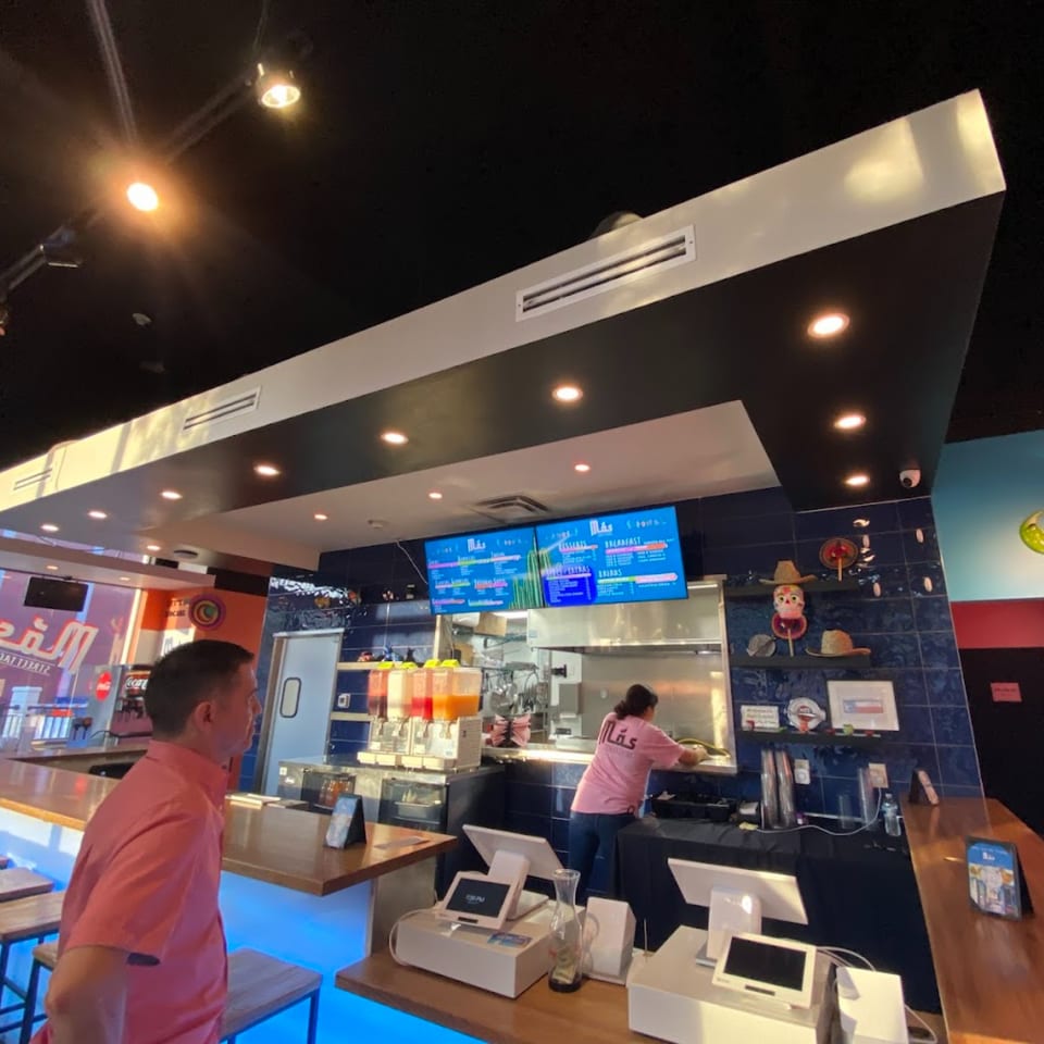 A customer stands at the counter of Mas Street Tacos, with staff working in the kitchen.