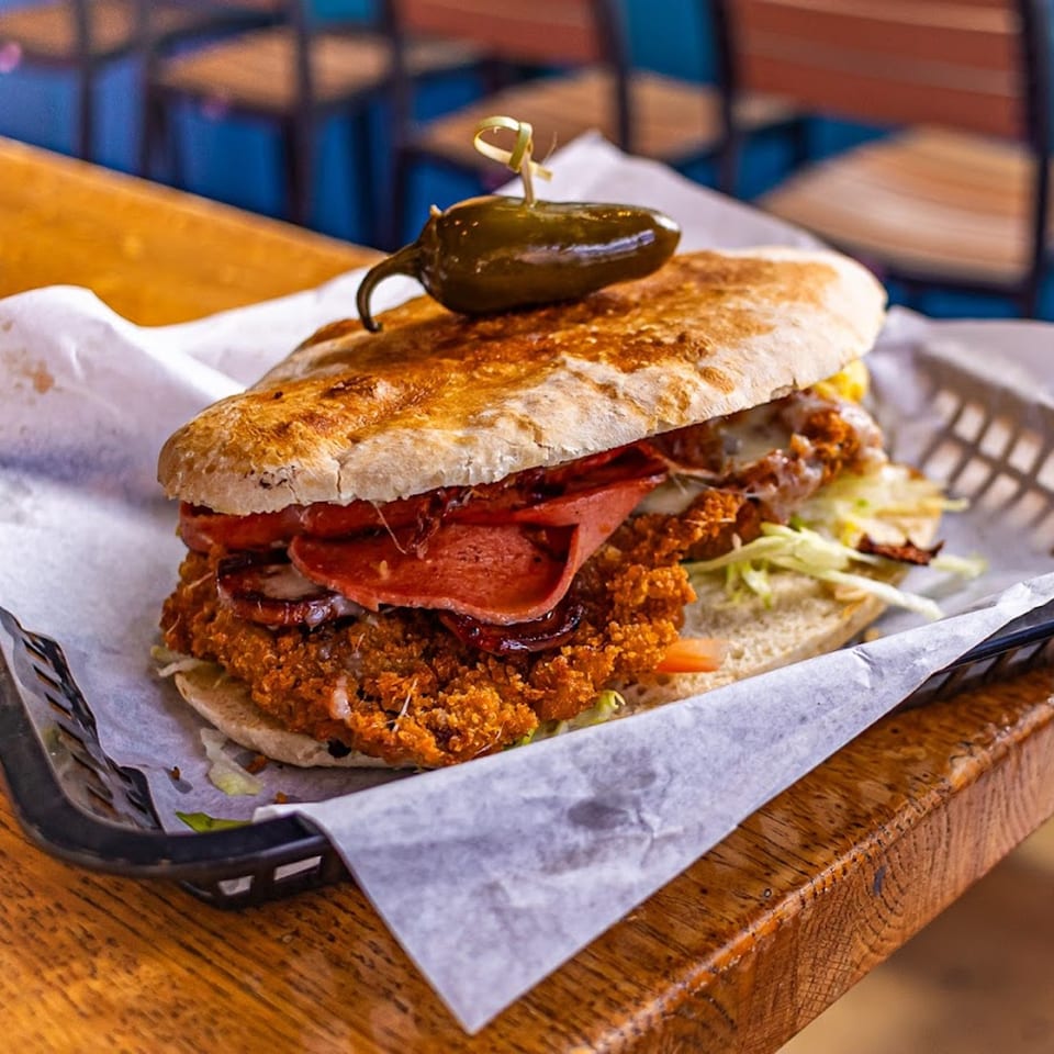A Mas Street Tacos torta, topped with a jalapeño, sits in a basket on a wooden table.