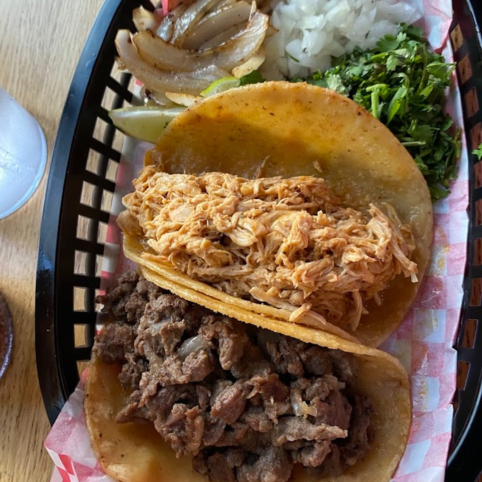 Two Mas Street Tacos, one chicken and one beef, with sides of cilantro, onions, and limes.