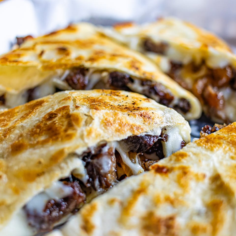 Close-up of several golden-brown quesadillas filled with melted cheese and dark meat, likely from Mas Street Tacos.