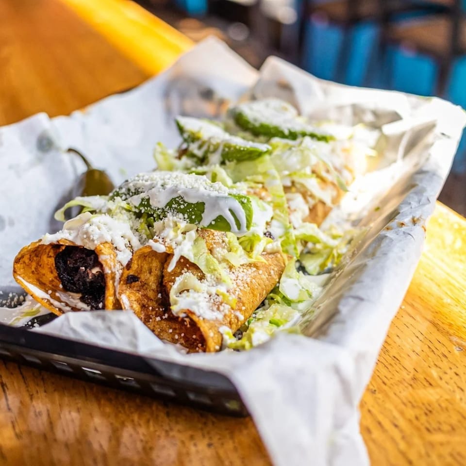 Three Mas Street Tacos, topped with lettuce, cheese, and sour cream, served in a basket.